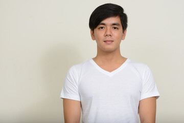 Portrait of young handsome Asian man against white background
