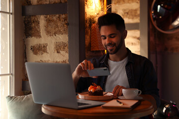 Young blogger taking picture of dessert at table in cafe