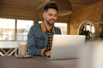 Young blogger working with laptop at table in cafe