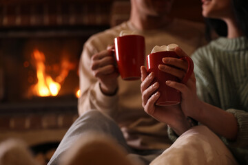 Lovely couple with delicious cocoa near burning fireplace at home, closeup. Winter vacation