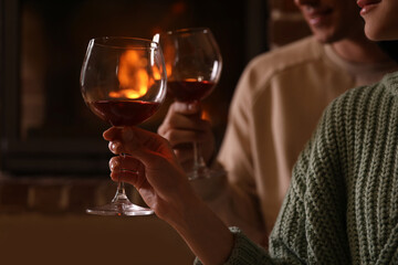 Lovely couple with glasses of wine near fireplace indoors, closeup. Winter vacation