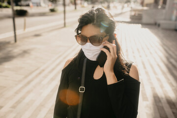 A female wearing a face mask, using her cellphone while standing by a red phonebooth
