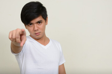 Portrait of young handsome Asian man against white background
