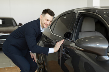 Fototapeta na wymiar Handsome young businessman in classic blue suit is smiling while examining car in a motor show