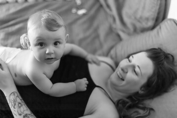 Mother and baby son joyful intimacy. Baby lying on his mother's chest and looking at camera with a funny, surprised expression. Black and white pic