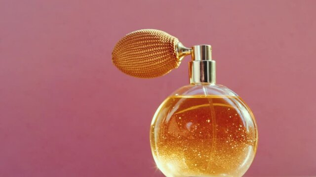 Luxury golden perfume bottle and shining light flares on pink background, glamorous fragrance scent as perfumery product for cosmetic and beauty brand, stock footage
