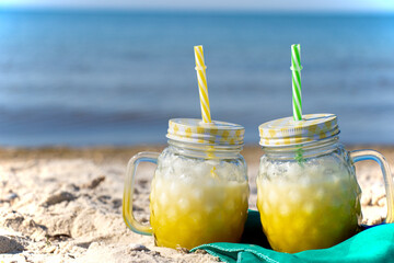 A yellow cocktail in a fashionable mug stands on the seashore on a green cloth. Sunny day, golden...