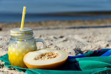 A yellow cocktail in a fashionable mug stands on the seashore on a green cloth. Melon smoothie. Healthy drink.