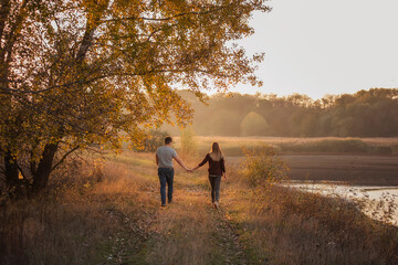 A young man and a girl are walking in the autumn forest. Happy lovers hold hands, hug each other,...