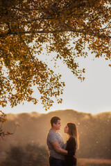 A young man and a girl are walking in the autumn forest. Happy lovers hold hands, hug each other, kiss, spend time together. Traveling during the cold season, on weekend days. Couple in love forever