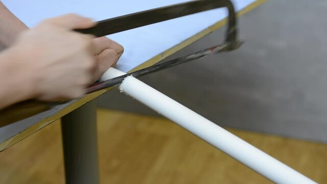 A man's hand using a tool hacksaw cuts off the PVC pipe.