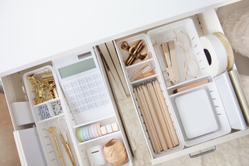 The gold stationery is neatly arranged in white containers in the drawers of the nightstand. Storage and tidying up the workplace.