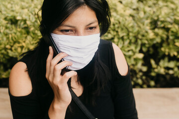 A female wearing a face mask, using her cellphone while standing by a red phonebooth