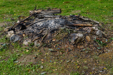 Coal and ash, surrounded by large stones, left after a fire in the garden on a lawn with green grass.