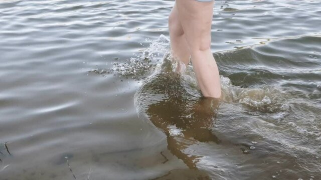 woman caucasian legs walking barefoot in a shallow stream, close view.