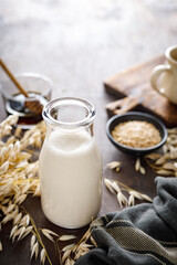 Obraz na płótnie Canvas Vegan oat milk in glass bottle and ingredients for cooking. Healthy vegetarian non-dairy drink or beverage. Alternative milk