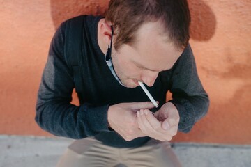 Closeup shot of a caucasian man lighting a cigarette with a  lowered a face mask