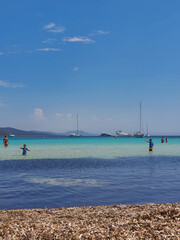 Błękitne morze ze statkami, żaglówkami oraz moczącymi sie w wodzie turystami w ciepły, letni, słoneczny dzień