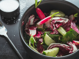 Spring vegetable salad in a black bowl with sea salt on the background.