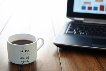 coffee cup with  love message on a wooden table and a computer out of focus in the background
