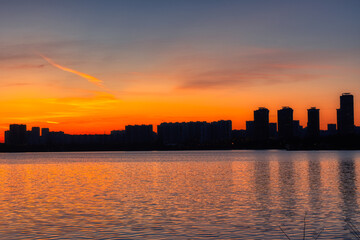 Silhouette of urban buildings on the background of an orange sunset reflected in the water of the bay