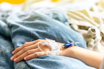 Focus on the hand of a patient in hospital ward on bed during dosing of intravenous saline