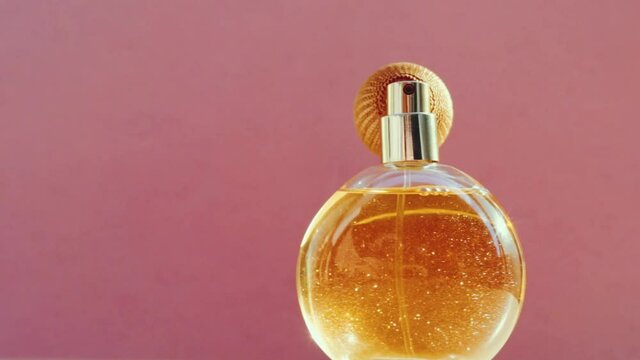 Luxury golden perfume bottle and shining light flares on pink background, glamorous fragrance scent as perfumery product for cosmetic and beauty brand, stock footage
