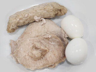 Pieces of healthy boiled fresh chicken pork breast serving with boiled egg and sausage on white plate, homemade restaurant, menu advertisement, food stylist backgrounds