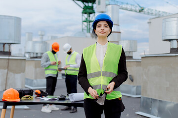 On construction site beautiful smiling lady engineer on the rooftop of building she wearing safety helmet, behind her are two co-workers