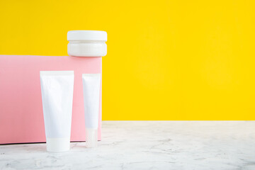Three white packages for cosmetic products on a pink cube and a yellow background. Creative layout.