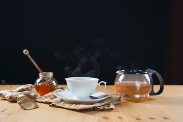 Cup of hot ginger tea with honey with steam from cup on wooden table over black background. the concept of natural medicine.