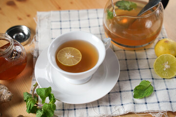 Top view of cup of hot ginger tea with honey, lemon and mint with steam from cup on wooden table over black background. the concept of natural medicine.