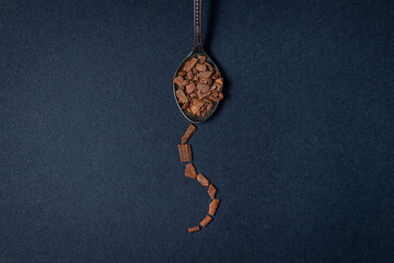 Cinnamon on a black background. A spoonful of crushed cinnamon. Next to the spoon, a path of...