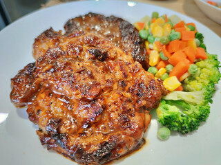 Sliced Grilled organic pork, beef Ribeye steak decorated with various colorful vegetables dressing corn carrot peas lemon serving on white plate on wooden table, One famous menu of secret recipe from 