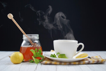 Cup of hot honey lemon tea with mint with steam from cup on wooden table over black background. the concept of natural medicine.