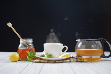 Cup of hot honey lemon tea with mint with steam from cup on wooden table over black background. the concept of natural medicine.