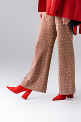 cropped view of trendy girl in beige trousers and red boots on grey