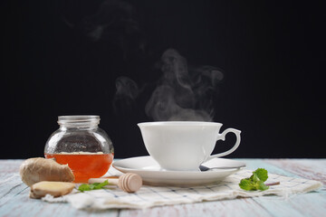 Cup of hot ginger tea with honey and mint with steam from cup on wooden table over black background. the concept of natural medicine.