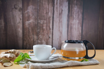 Cup of hot ginger tea with lemon and mint with steam from cup on wooden table. the concept of natural medicine.