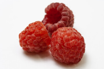 Three ripe raspberries isolated on a white background close-up. Fresh raspberries without sheets on the table. Macro shooting. Healthy and wholesome food concept