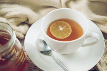 Cup of hot honey lemon tea and mint with steam from cup on wooden table with dressed in knitted warm winter scarf. the concept of natural medicine.
