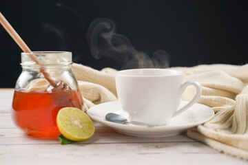 Cup of hot honey lemon tea and mint with steam from cup on wooden table with dressed in knitted warm winter scarf over black background. the concept of natural medicine.