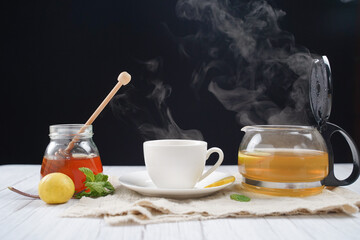 Cup of hot honey lemon tea with mint with steam from cup on wooden table over black background. the concept of natural medicine.