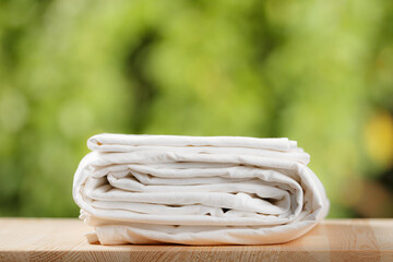 A stack of folded white bedding. Bed sheet set on blurred foliage background