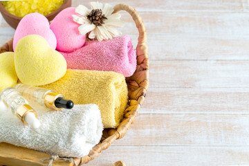 Relaxing bath accessories with yellow and pink heart shaped bath bombs, body brush, serum, palo santo, towels and flower on a wooden background. Relaxation, spa, beauty cosmetics for body treatment