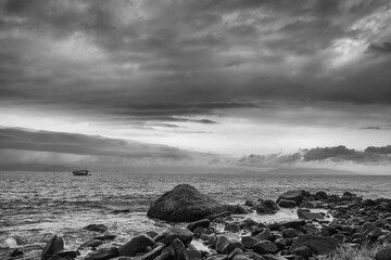 Greyscale shot of a boat in the sea with a cloudy dark sky over it