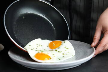 Woman putting tasty cooked eggs onto plate from frying pan at black table, closeup