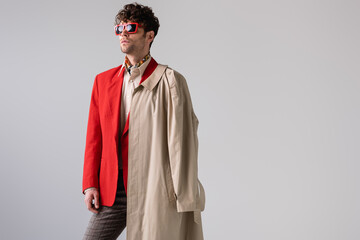 trendy man with trench coat on shoulder looking away isolated on grey