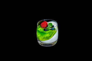 Homemade yogurt with green  berry jelly or yogurt in glasses is served with fresh strawberries, honeysuckle and mint leaves. Close up. Dark background.