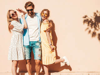 Group of young three stylish friends posing in the street. Fashion man and two cute girls dressed in casual summer clothes. Smiling models having fun in sunglasses.Cheerful women and guy going crazy